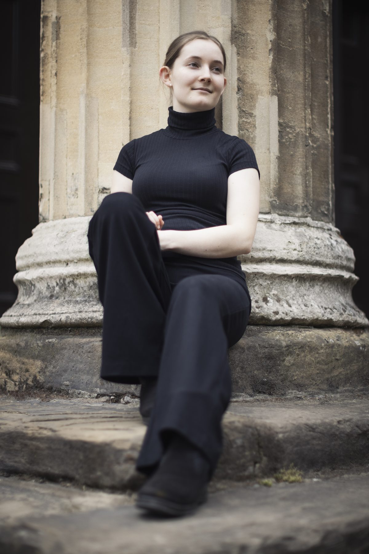 Alma Deutscher seated beside a stone column, photographed by Ben Ealovega
